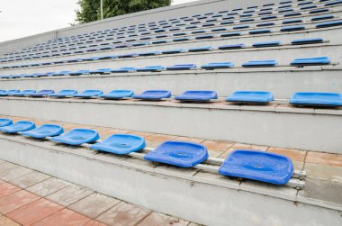 Stadyumda bir sürü boş koltuk var. Mavi sandalyelerin dokusu. Plastik koltuklar sıraya dizildi. Kirli ve tırmalanmış fan koltukları. Yağmurdan sonra tadium