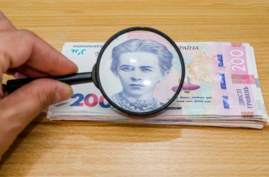 Büyüteçle Hryvnia 'yı kontrol etme fikri. Ukrayna 200 Hryvnia 'sı ve elinde büyüteçle bir kadın eli.