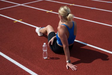 Koşu bandında oturup gülümseyen yorgun ve mutlu koşucu. Genç atletik koşucu antrenmandan sonra dinleniyor. Daha çok çalış, daha çok dinlen. Boşluğu kopyala.
