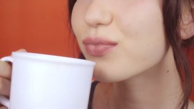 Parlak kırmızı arka planda muhteşem dudakları olan esmer bir kız. Kadın beyaz bardaktan bir içki içiyor, dudaklar kapalı..