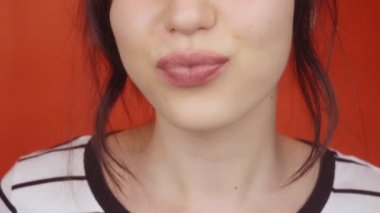 Parlak kırmızı arka planda muhteşem dudakları olan esmer bir kız. Mutlu kadın kameraya hava öpücüğü gönderiyor, dudaklar kapalı..