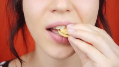Parlak kırmızı arka planda muhteşem dudakları olan genç bir kız. Küçük kurabiyeler yiyen kadın, yakın plan dudaklar..