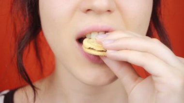 Parlak kırmızı arka planda muhteşem dudakları olan genç bir kız. Küçük kurabiyeler yiyen kadın, yakın plan dudaklar..