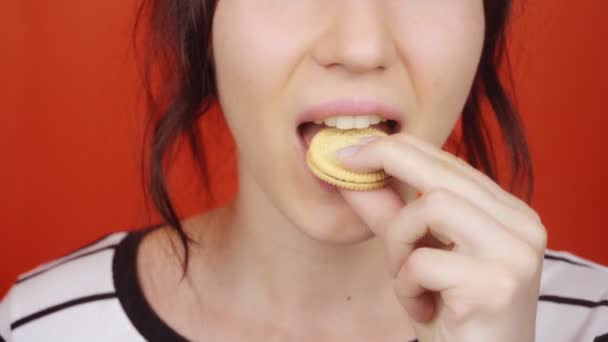 鮮やかな赤の背景に豪華な唇を持つ若い女の子 女性は小さなクッキーを食べます 唇のクローズアップ — ストック動画