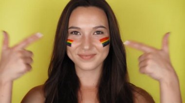 Yüzünde LGBT toplumsal bayrağı olan esmer bir kadın baş parmak işareti yapıyor. Jest gibi. Yüksek kaliteli görüntüler