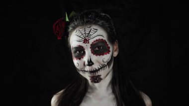 Meksika Ölüler Günü. Şeker kafalı, Cadılar Bayramı makyajlı genç bir kadın kameraya bakıyor ve gülümsüyor. Son derece yakın çekim. Mutlu Cadılar Bayramı.