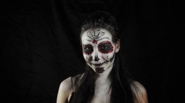 Cadılar Bayramı maskesi Calavera Catrina. Elinde gül olan bir kız. Meksika Ölüler Günü. Karanlık bir arka planda cadılar bayramı için korkunç renkli makyajlı genç bir kadının portresi. 4K. 