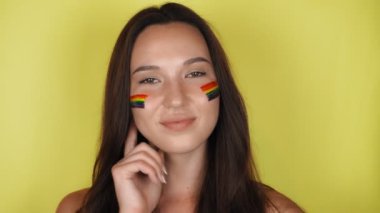 Yüzünde LGBT halk bayrağı olan esmer bir kadın dönüp kameraya bakıyor. Yüksek kalite 4k görüntü