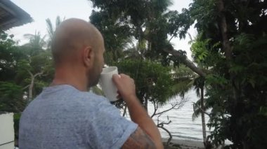 Genç bir adam arka planda güzel palmiye ağaçları üzerinde sıcak bir içecek içer..