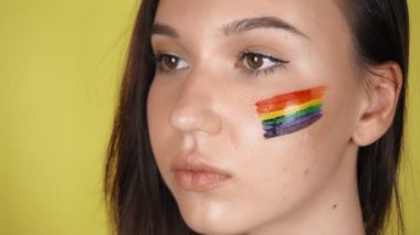Yüzünde gökkuşağı deseni olan bir kadın. Yüzünde LGBT bayrağı var. Sarı arka plan. Yüksek kalite 4k görüntü