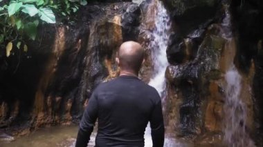 Bir adam ormanda küçük bir şelaleye bakar..