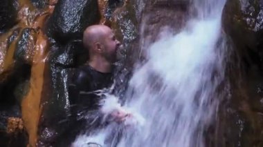 Bir adam şelalede yüzünü yıkar. Adamın üzerine büyük bir su akıntısı düşüyor..