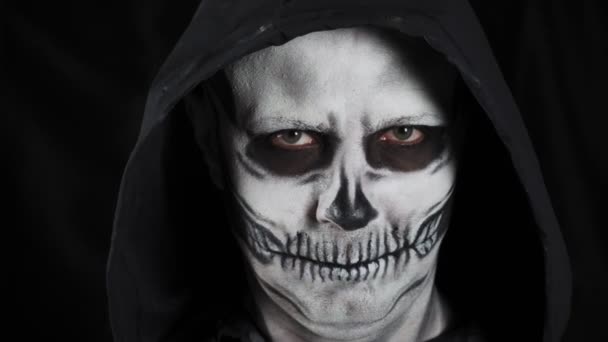 有化妆骷髅和黑色头罩的男人在黑暗的背景 一个男人脱下帽子 露出骷髅 万圣节或恐怖主题 — 图库视频影像