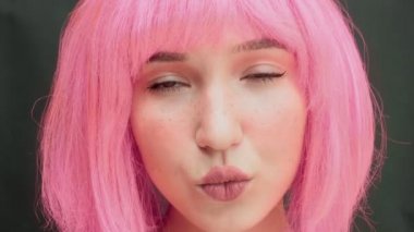 Pembe saçlı bir kadın yukarı bakar ve çabucak göz kırpar. Çocukça ve saf bir bakış. Karanlık arka plan. Yüksek kalite 4k görüntü