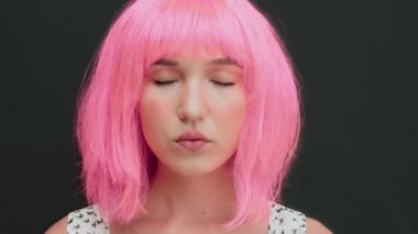 Pembe saçlı bir kadın gözlerini açar ve kameraya bakar. Karanlık arka plan. Yüksek kalite 4k video