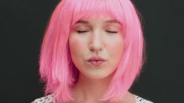 Pembe saçlı bir kadın gözlerini açar ve kameraya bakar. Karanlık arka plan. Yüksek kalite 4k video