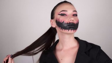 Korkunç cadılar bayramı makyajlı güzel bir kadın. Gri arka planda bir kadın saçını elinde büker ve kameraya bakar.. 