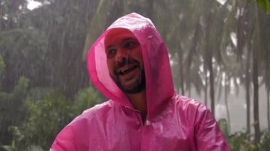 Pembe yağmurluk giyen yetişkin bir adam tropikal yağmurdan hoşlanır. Ağır çekim. Yüksek kaliteli FullHD görüntüler