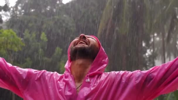 ピンクのレインコートを着た大人の男が熱帯雨を楽しんでいます スローモーション 高品質のフルHd映像 — ストック動画