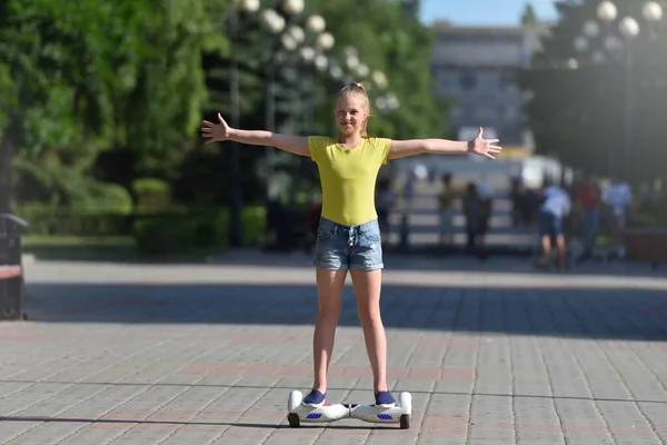 Gadis remaja yang gembira mengendarai hoverboard di taman musim panas dengan tangan terbuka lebar — Stok Foto