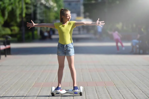 Boldog lány gyermek lovaglás egy hoverboard egy nyári parkban, és élvezi a napfényt — Stock Fotó