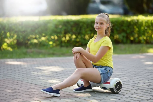 Usmívající se dívka dítě sedí na hoverboard v letním parku relaxační — Stock fotografie