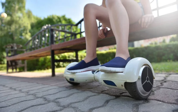 Voeten van een meisje kind op een hoverboard terwijl ontspannen op een bank in een park — Stockfoto