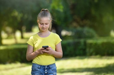 Şirin bir kız çocuğu, arka plandaki akıllı telefondan fotokopi alanı olan ağaçlardan bir mesaj okur.