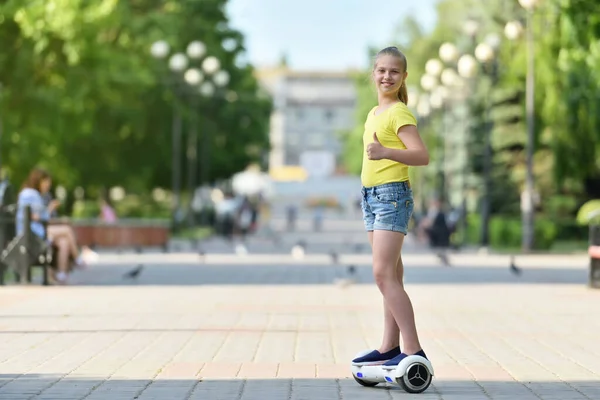 Meisje kind rijden een hoverboard op een zonnige dag en tonen een vinger als kijken naar de camera — Stockfoto