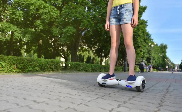 Ein Mädchen reitet mit einem elektrischen Hoverboard in einem Park auf einem gefliesten Bürgersteig — Stockfoto