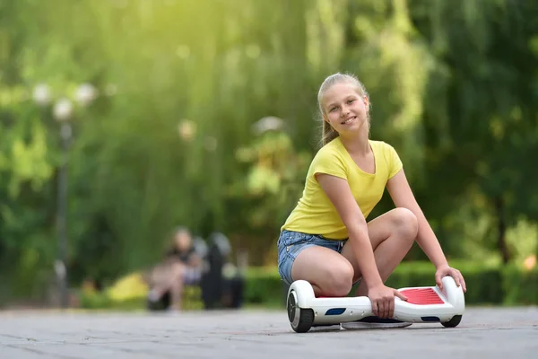 Nettes junges Mädchen mit einem Lächeln und einem Hoverboard vor dem Hintergrund eines grünen Parks — Stockfoto