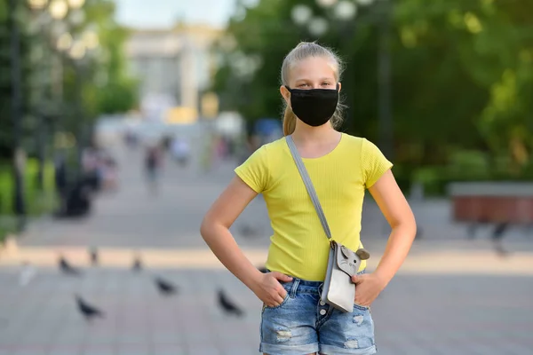 COVID-19パンデミックの間の夏の公園の背景に黒い保護マスクの女の子の子供は、カメラで悲しいように見えます — ストック写真
