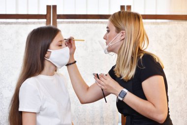 Kına kaş boyası. Makyöz, Covid-19 salgını sırasında koruyucu maske takmış genç bir kızın kaşlarını boyuyor.