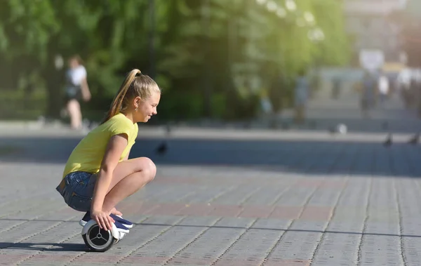 Κορίτσι παιδί βόλτες, ενώ κάθεται σε ένα hoverboard σε ένα καλοκαιρινό πάρκο, ευτυχισμένη και χαρούμενη — Φωτογραφία Αρχείου