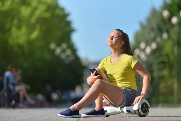 스마트폰을 들고 공원을 산책하면서 여름 햇살을 즐기는 귀여운 소녀. — 스톡 사진