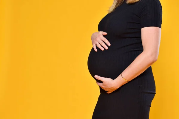 Kobieta w ciąży trzyma brzuch na żółtym tle — Zdjęcie stockowe