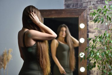 Uzun saçlı esmer kız aynaya ampullerle bakıyor.