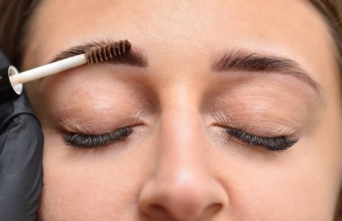 Kınayla ve genç bir kadının yüzüyle kaş boyama işlemi.