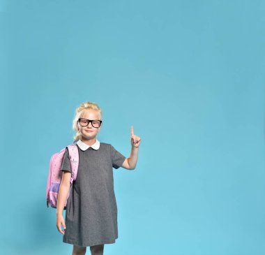 Sevimli ilkokul kızı mavi arka planda boş alana parmak gösteriyor.