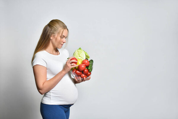 Young pregnant woman holding a bowl of vegetables on a gray background, healthy eating and pregnancy