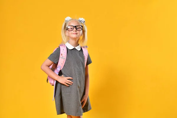 Cute little school girl posing with backpack on yellow background