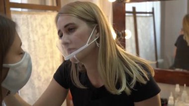 Koruyucu maskeli genç kız ve güzellik uzmanı kaşlarını cımbızla koparıyor.