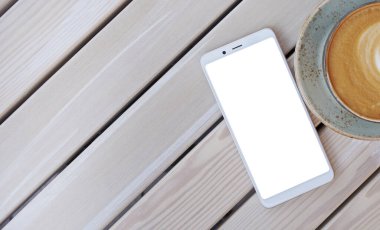 Kafedeki ahşap masada üzerinde kahve fincanı olan kişiselleştirilmiş metin için beyaz ekranlı akıllı telefon.