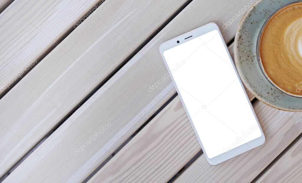 Smartphone with white screen for customized text on wooden table in cafe with mug of coffee