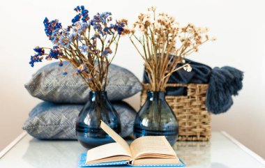 Konforlu ev dekorasyonu: açık kitap, çiçekli vazo, yastık ve ekoseli beyaz bir masa. Uzaktan eğitim. Karantina konsepti: