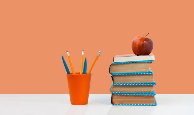 Okula, kitap yığınına ve pembe turuncu arka planlı beyaz masada kırmızı elmaya. Uzaktan eğitim. Karantina konsepti: