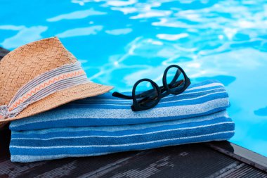 Eski yaz hasır hasır hasır plaj şapkası, güneş gözlükleri, yüzme havuzunun yanındaki mavi havlu, tropik arka plan.