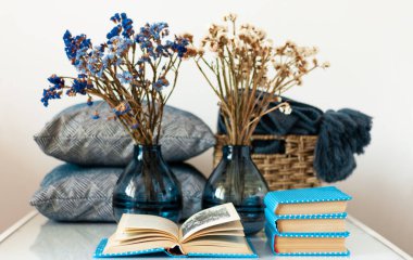 Konforlu ev dekorasyonu: bir yığın kitap, beyaz bir masanın üzerinde çiçekli vazo. Uzaktan eğitim. Karantina konsepti: