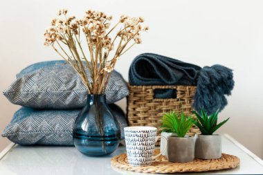 Konforlu ev dekorasyonu: bir fincan kahve, hasır tezgahtaki saksılarda bitkiler, beyaz masadaki çiçekli vazolar. Uzak ev karantina konsepti evde kalma