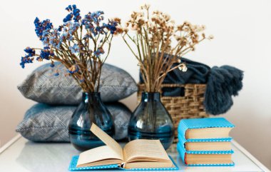 Konforlu ev dekorasyonu: bir yığın kitap, beyaz bir masanın üzerinde çiçekli vazo. Uzaktan eğitim. Karantina konsepti: